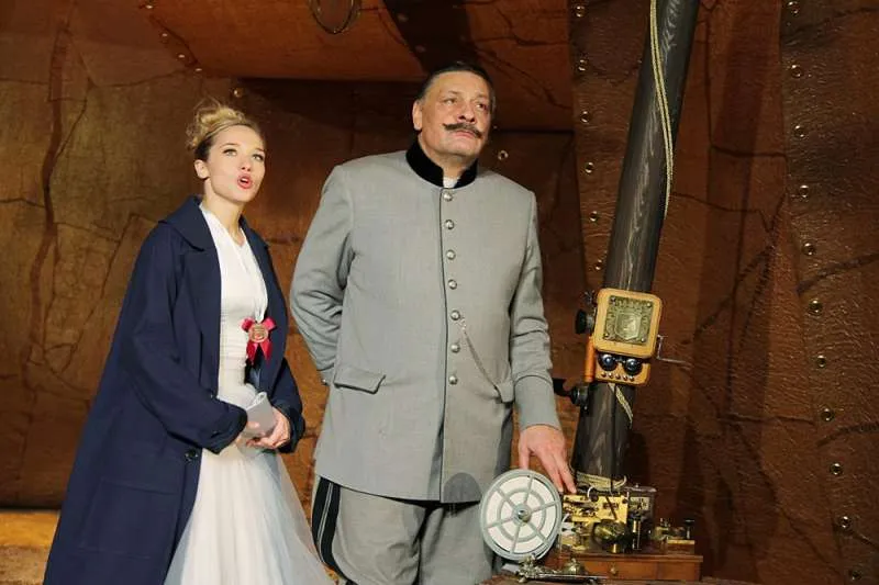 Режиссер Роман Самгин (к слову, прекрасный театральный комедиограф) вероятно впервые в России обращается к этому произведению. В роли великого герцога, принца регента вымышленной страны Карпатии - Народный артист России Дмитрий Назаров. Любимец публики, обаятельный, ироничный артист блистает в этой постановке, которая к счастью позволяет демонстрировать ему лучшие грани своего таланта. Нельзя не отметить его прекрасный дуэт (наверняка, не в пример Оливье - Монро, впрочем, на экране в итоге смотрящимися не плохо) с Ксенией Тепловой, которая после яркого дебюта и нескольких больших и выразительных ролей на сцене Художественного театра несколько ушла в тень (последняя по сути серьезная ее работа датировалась 2012-м годом, хотя была одна премьера и в 2015-м), но наконец в новом спектакле предстает во всем своем блеске и очаровании, с первых минут очаровывая зрителя своей лучезарностью и обаянием.